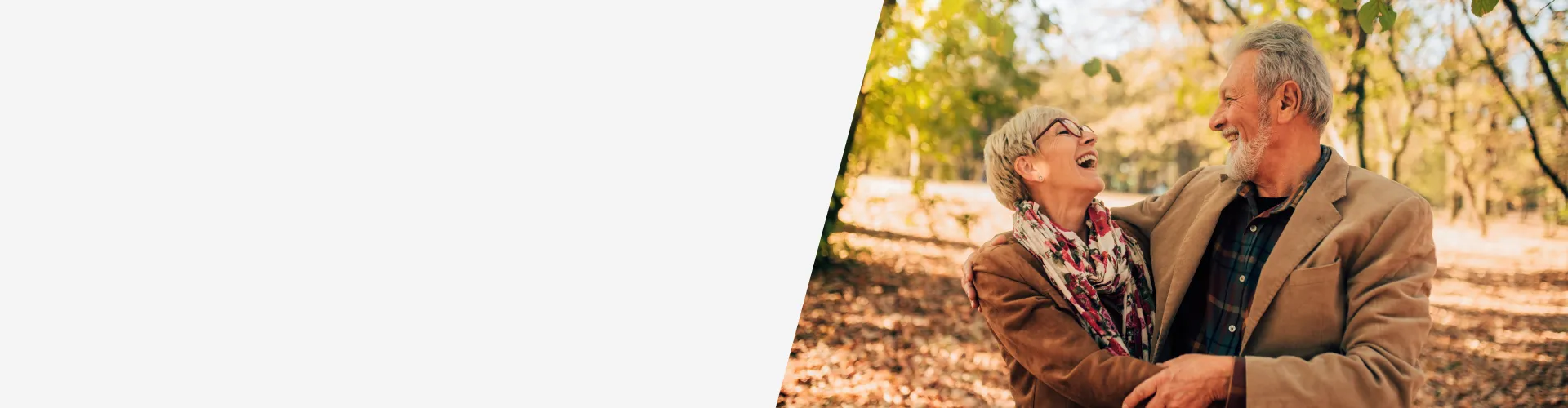 Pareja adulta abrazada en un parque durante el otoño, rodeada de árboles y hojas secas, concepto de planes de pensiones y jubilación