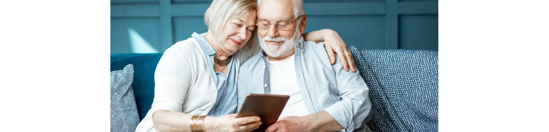 Dos personas sentadas en un sofá, abrazadas y mirando una tablet, concepto de planificación financiera y ahorro para la jubilación