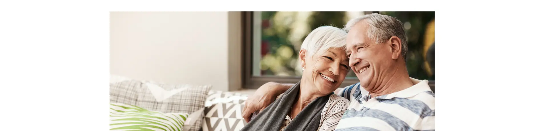 Dos personas sentadas en un sofá junto a una ventana, en un ambiente hogareño, concepto de tranquilidad y planificación financiera para la jubilación
