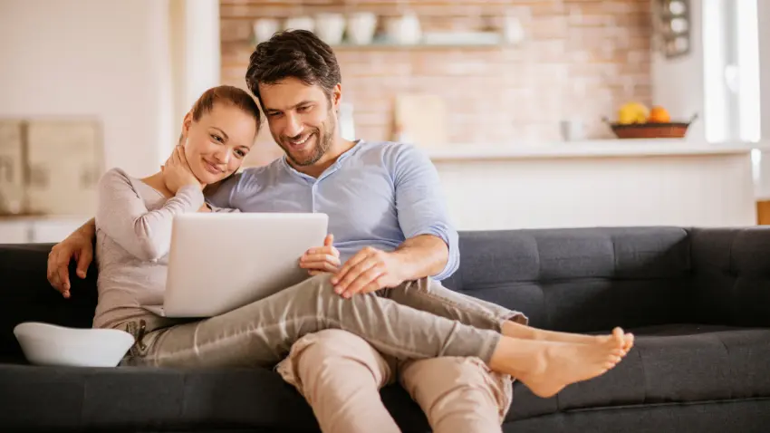 Un hombre y una mujer sentados en un sofá, usando un ordenador portátil juntos.