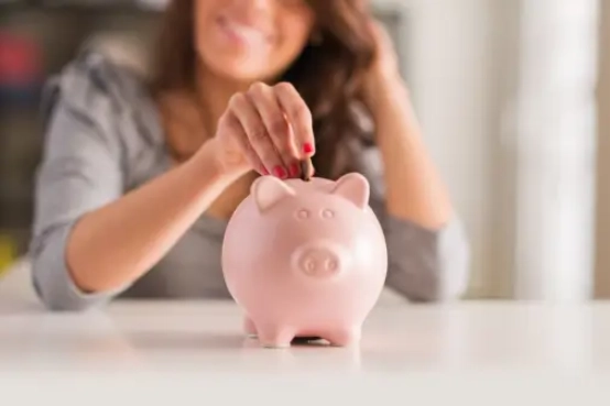 Persona introduciendo una moneda en una hucha como símbolo de ahorro y planificación financiera.