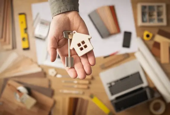Persona mostrando una llave de casa junto a un modelo de casa de madera, simbolizando la compra de una vivienda.