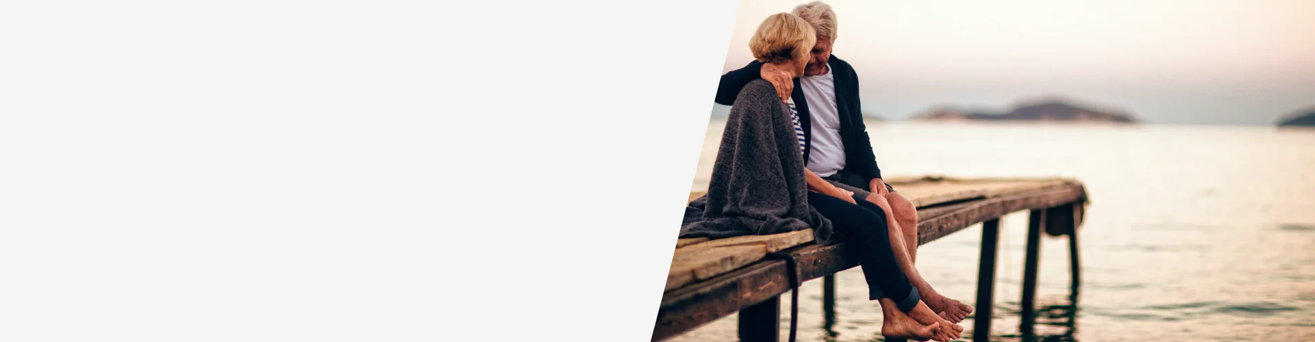 Dos personas sentadas en un muelle frente al mar al atardecer, con manta sobre las piernas, concepto de tranquilidad, seguridad financiera y rentas vitalicias