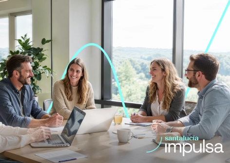 Reunión de trabajo en oficina luminosa con ordenadores portátiles y documentos sobre la mesa, colaboración en proyecto de innovación empresarial Santalucía Impulsa