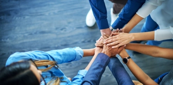 Equipo uniendo manos en señal de colaboración y trabajo en equipo sobre superficie de madera