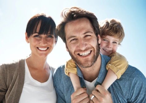 Familia disfrutando de un día soleado al aire libre, con un adulto cargando a un niño sobre los hombros