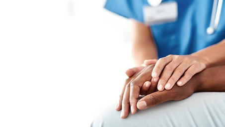 Profesional sanitario con uniforme azul sosteniendo la mano de una persona, gesto de apoyo y cuidado