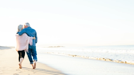 Pareja caminando descalza por la orilla de la playa con el mar y horizonte despejado.