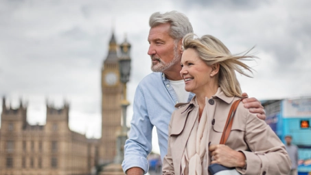 Pareja abrazada en primer plano con el Big Ben y edificios históricos de Londres al fondo.