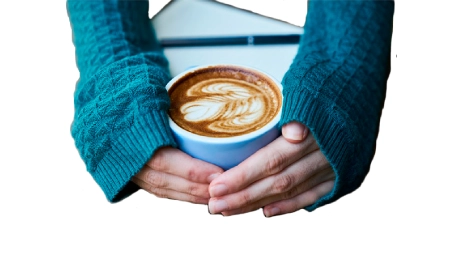 Manos con suéter azul sujetando taza de café con arte latte, sobre mesa blanca