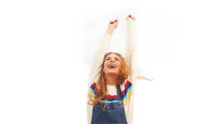 Persona con brazos levantados vistiendo camiseta clara y peto vaquero, sobre fondo blanco