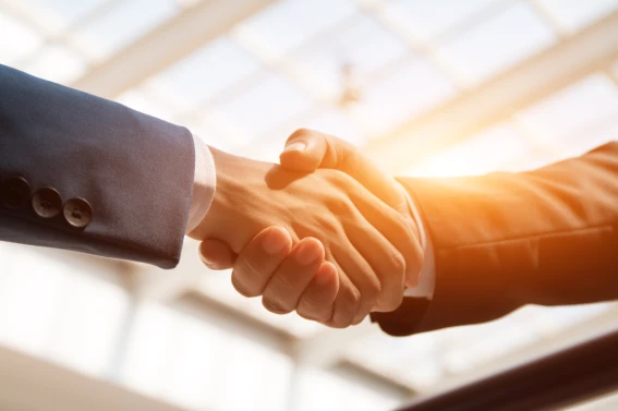 Dos personas estrechando la mano en señal de acuerdo comercial, cierre de negocio o inversión segura, con luz natural en fondo corporativo
