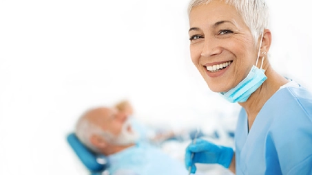 Profesional sanitario atendiendo a paciente en consulta dental, revisión bucodental con equipo médico y guantes de protección