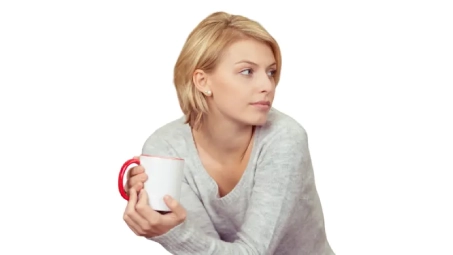 Persona sosteniendo una taza blanca con borde rojo, vestida con jersey gris, en posición relajada sobre fondo neutro