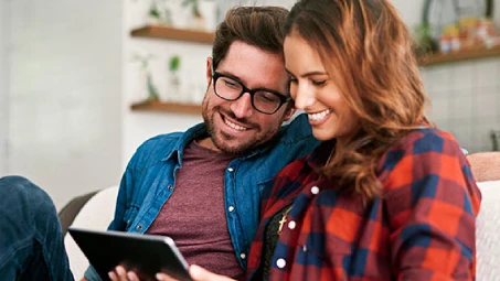 Dos personas sentadas en un sofá utilizando una tablet, concepto de gestión online de seguros desde el hogar