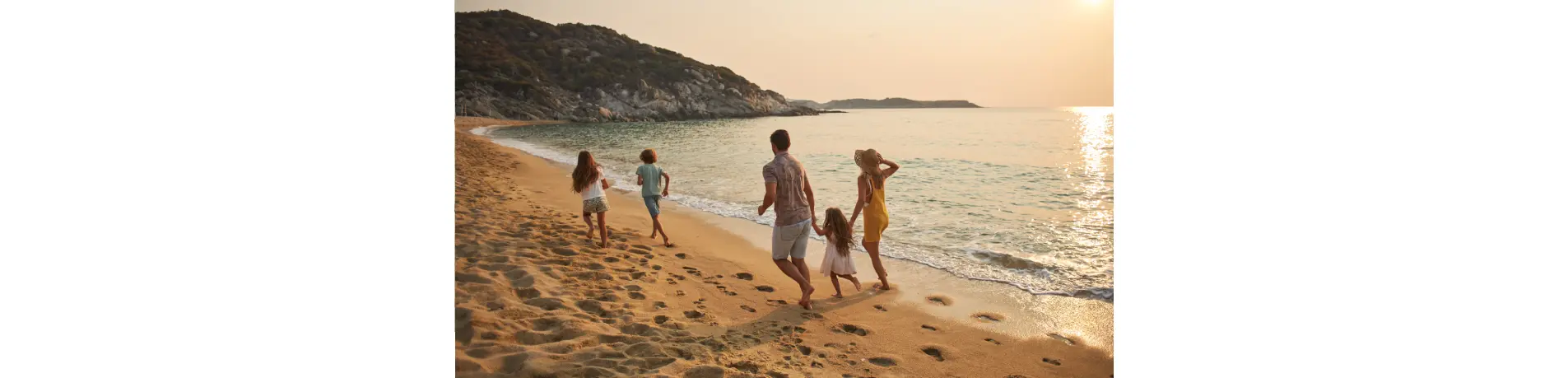 Familia caminando por la playa al atardecer junto al mar, dejando huellas en la arena