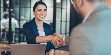 Personas en reunión profesional estrechando manos sobre escritorio con portátil y documentos