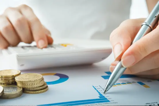Persona realizando cálculos financieros con calculadora, gráficos y monedas sobre la mesa