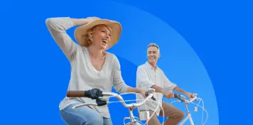 Dos personas montando en bicicleta sobre un fondo azul, una de ellas con sombrero y gesto dinámico mientras avanzan