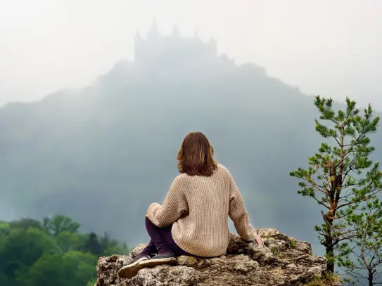 Persona sentada sobre una roca en un entorno natural con vistas a la montaña, imagen asociada a sostenibilidad, respeto por el entorno y compromiso del Grupo SANTALUCÍA.