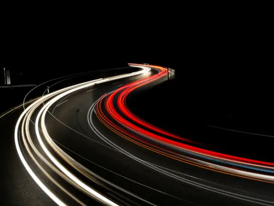 Trazas de luz en movimiento sobre una carretera en curva, imagen que representa la innovación, el avance tecnológico y la transformación del Grupo SANTALUCÍA.